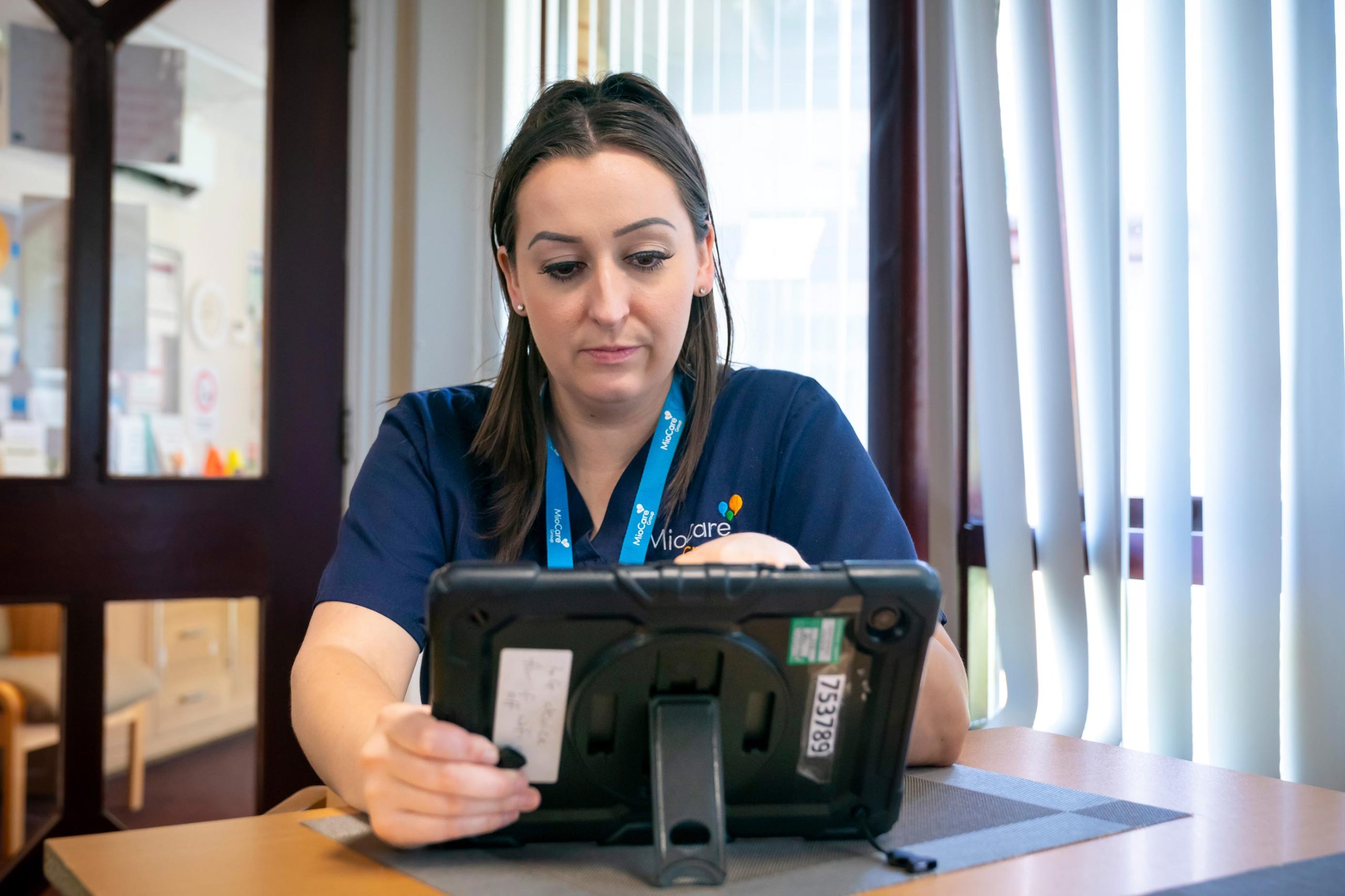 MioCare care worker using a digital tablet while seated at a table.